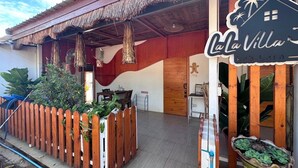 Une clôture en bois agrémentée de plantes, un toit de chaume et une enseigne indiquant « La Villa Koh Larn ».