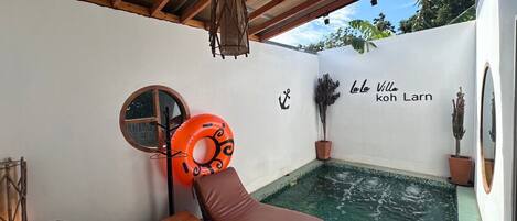 A small pool area with a lounge chair, a round table, and a potted plant.