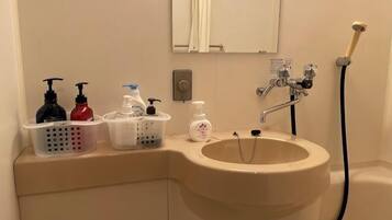 A bathroom with a sink, hand soap dispensers, a shower head, and a mirror.