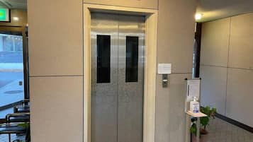 An elevator with a metallic finish, a sign above it, and a potted plant beside it.