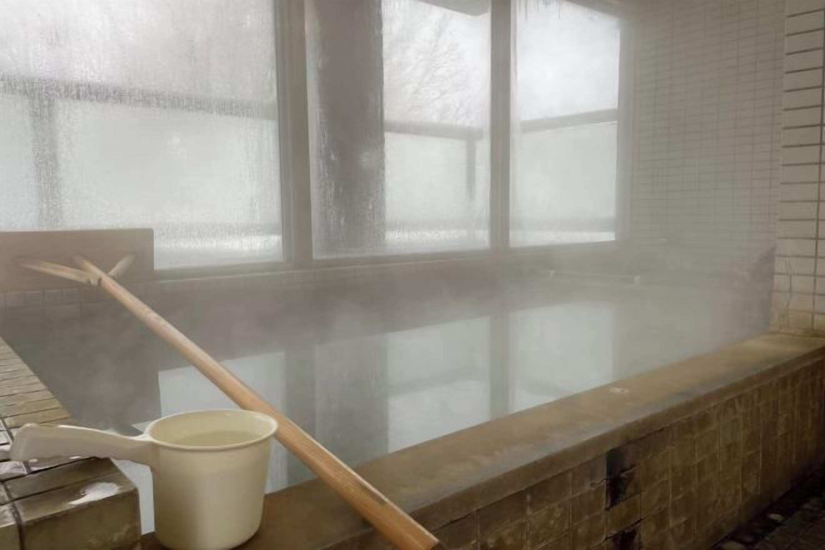 A steam room with a wooden bench, a white bucket, and a wooden stick.