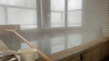 A steam room with a wooden bench, a white bucket, and a wooden stick.