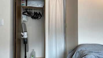 Una habitación de hotel con cama, un armario con ropa colgada y una ventana con cortina.