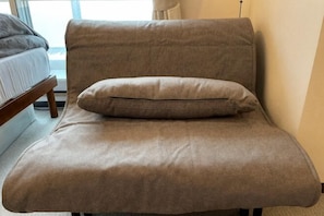A brown sofa with a cushion in a room with a wooden floor and a window.