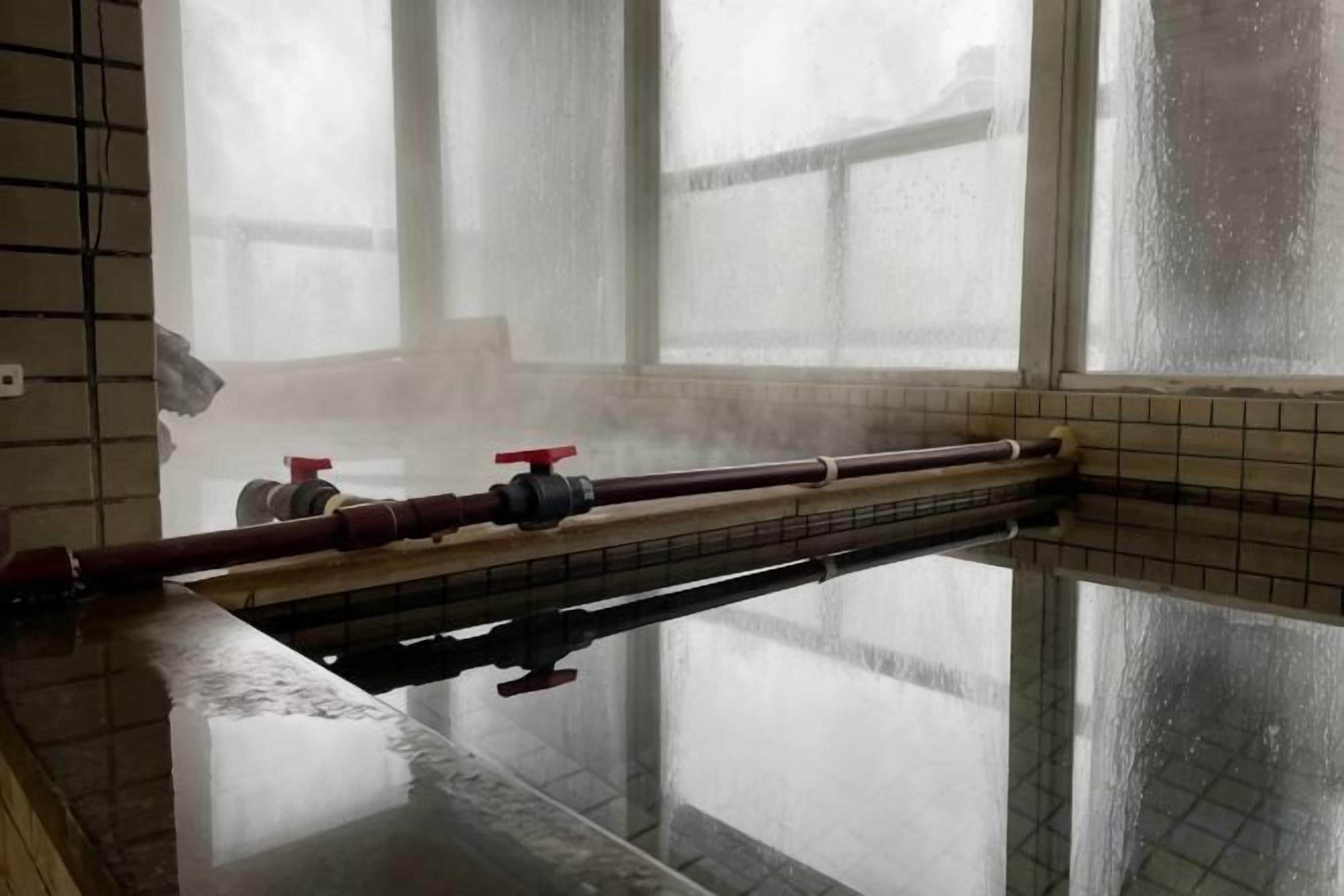 A bathroom with a glass partition, a bathtub, and a window with condensation.