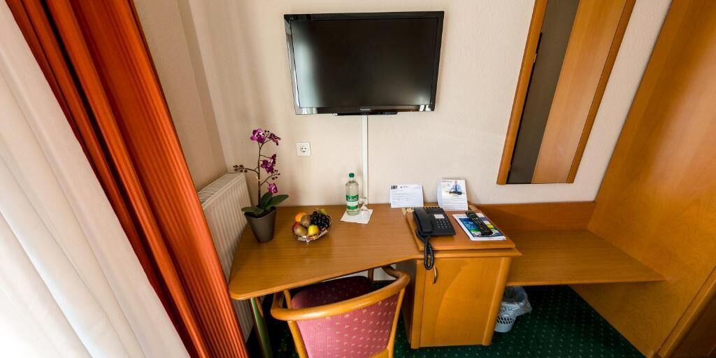 Ein gemütlicher Raum mit Flachbildfernseher an der Wand, einem kleinen Holztisch mit Obstschale, einem Sessel und einem Telefon.