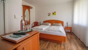 Ein Hotelzimmer mit Holzboden, einem Bett mit weißer Bettwäsche, einem Schreibtisch mit Fernbedienung, einem Spiegel und einem Nachttisch mit Lampe.