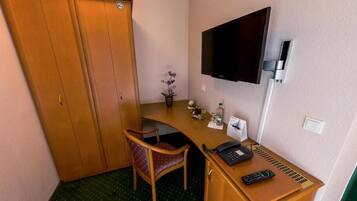 Une chambre d’hôtel compacte, dotée d’un bureau en bois, d’une chaise, d’un téléviseur fixé au mur et d’une petite plante en pot.