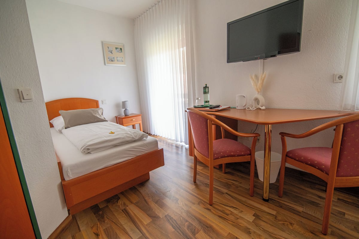Habitación de hotel con cama, escritorio, dos sillas, televisor y ventana con cortinas.