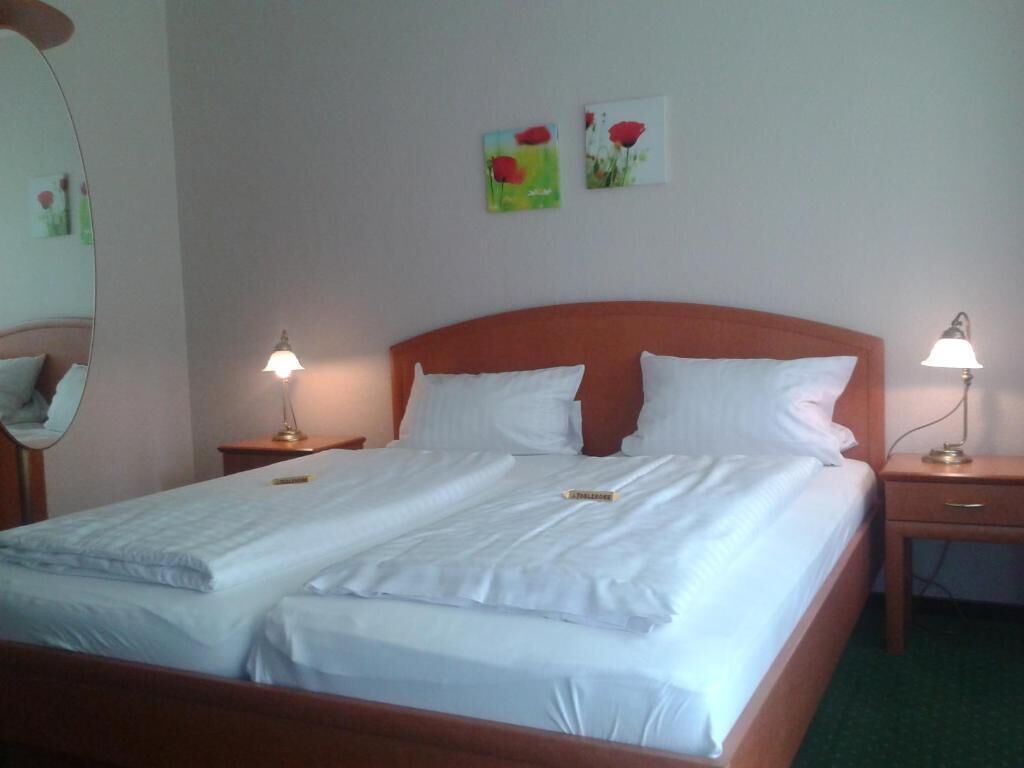 A neatly made bed with white linens, two bedside lamps, and two paintings on the wall.