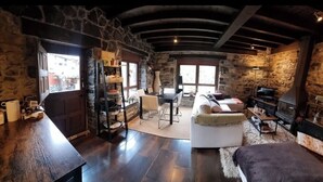Un interior rústico de piedra con una mesa de madera, un sofá, una chimenea y un televisor.
