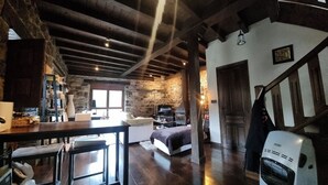 Un interior rústico con vigas de madera a la vista, una pared de piedra, una cama, una zona de bar y una escalera.