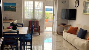 A living room with a sofa, TV, and a dining area with chairs and a table. - Casa Mariuccia Cozy apartment near the waterfront Valencia (Alghero)