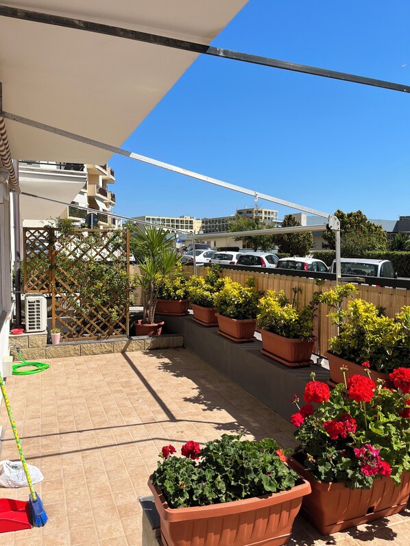 A rooftop terrace with potted plants and a view of parked cars and buildings.
