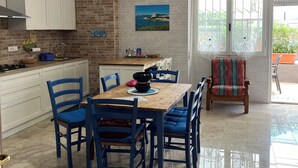 A kitchen with white cabinets, a brick backsplash, and a dining area with blue chairs and a wooden table. - Casa Mariuccia Cozy apartment near the waterfront Valencia (Alghero)