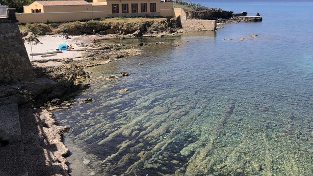 A coastal building with a clear view of the sea, a rocky shoreline, and a sandy beach. - Casa Mariuccia Cozy apartment near the waterfront Valencia (Alghero)