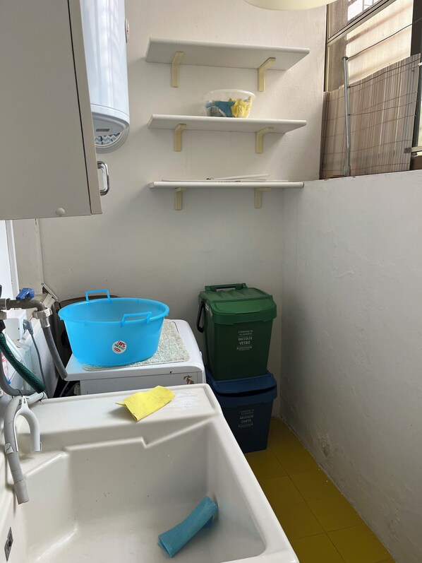 Une petite salle de bain avec un lavabo blanc, un bac bleu et deux poubelles.