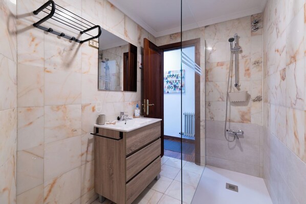A modern bathroom with a wooden vanity, a glass shower enclosure, and marble tiles. - The Sun Terrace (Vigo)