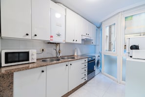 Una cocina compacta con armarios blancos, microondas, pileta, lavadora y un refrigerador pequeño.