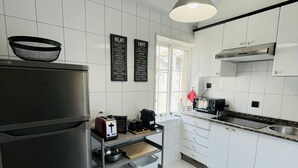 Een moderne keuken met witte kastjes, een roestvrijstalen koelkast, een koffiezetapparaat en een hangende lamp.