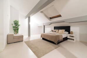 A modern bedroom with a skylight, a bed with a headboard, a bedside table, a nightstand, a sofa, and a potted plant. - Elegant Duplex Penthouse with Parking (Vigo)