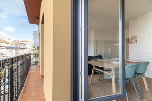 Un balcon doté d’une rambarde en métal et d’une porte-fenêtre coulissante donnant sur un coin repas avec une table et des chaises.