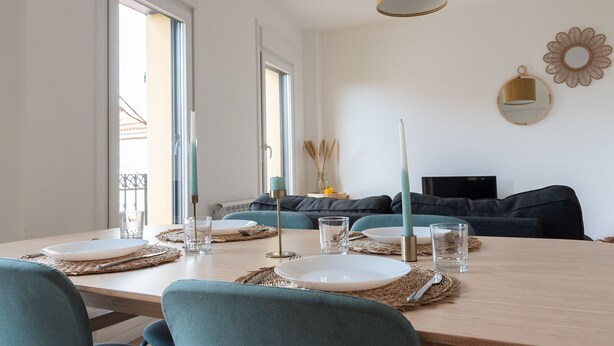 A dining area with a table set for four, a sofa in the background, and a TV on a stand. - Balcony (Vigo)