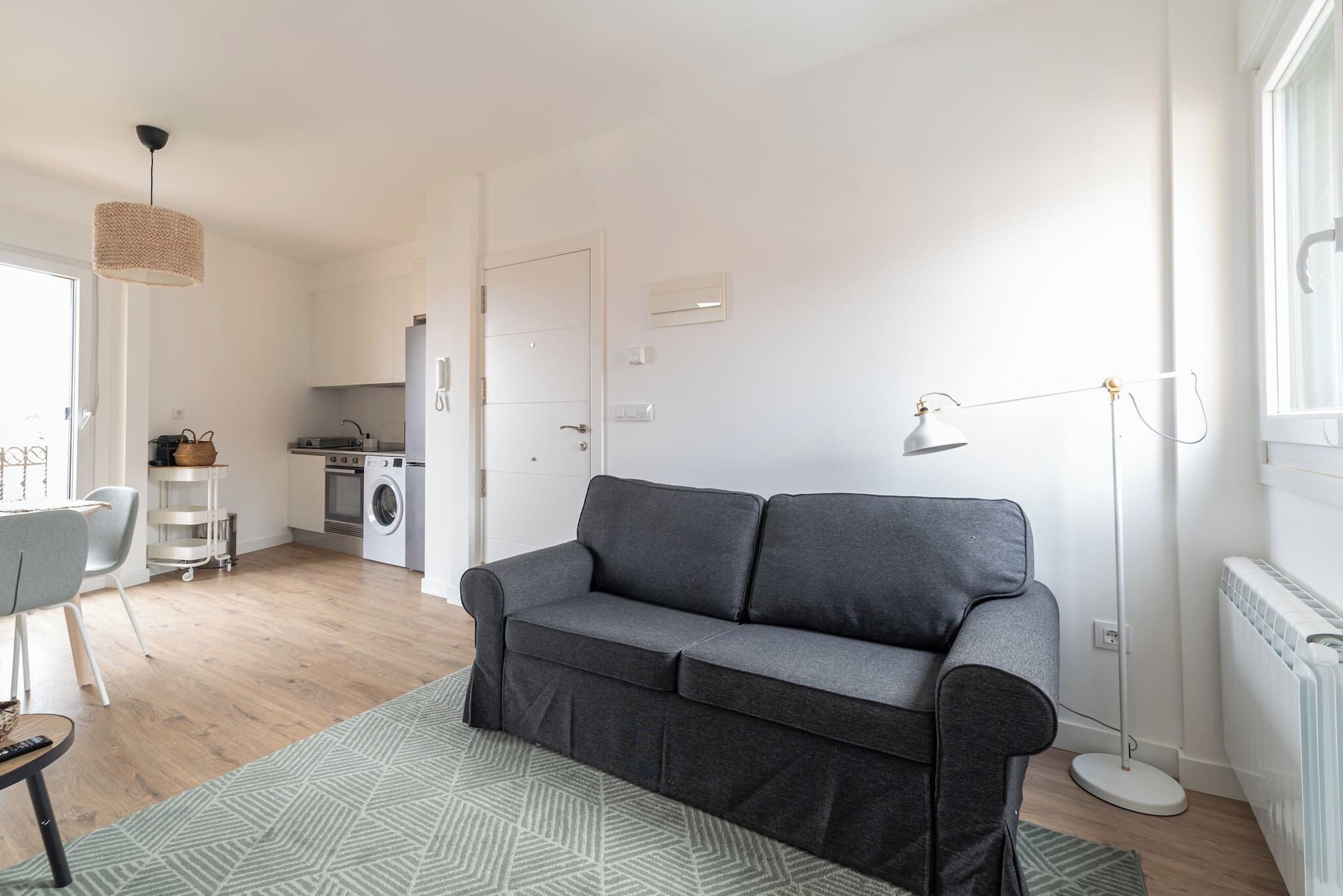 Una sala moderna con un sofá gris, un comedor con mesa y sillas, una cocina equipada y un área de lavandería.