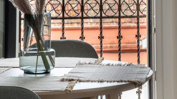 A balcony with a table, chairs, and a vase with dried plants.