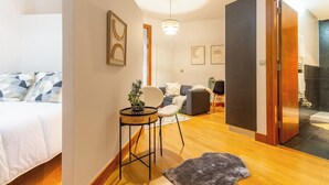 Une chambre d’hôtel moderne, équipée d’un lit, d  ’une petite table avec une plante, d’un canapé et d’une salle de bain visible à travers une porte ouverte.