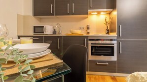 Une cuisine moderne avec des meubles de couleur sombre, un four à micro-ondes, un four traditionnel et une table à manger dressée avec des assiettes et un verre.