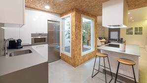 Une cuisine moderne avec un plafond en bois, des appareils en acier inoxydable, une grande fenêtre et un coin bar avec des tabourets.