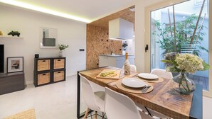 Un espace repas moderne avec une table en bois dressée pour deux personnes, un vase de fleurs et une vue sur la ville grâce à de grandes fenêtres.