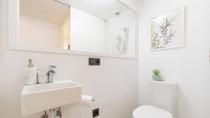 Une salle de bain moderne avec un lavabo blanc, des toilettes et un grand miroir. Deux reproductions botaniques encadrées ornent le mur.