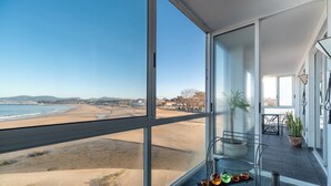 En balkon med frit udsyn til stranden og havet, en potteplante og et lille bord med pynt.