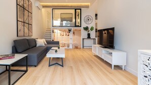 Una sala de estar moderna con un sofá gris, una mesa de centro, un televisor y una escalera que conduce a un nivel superior.