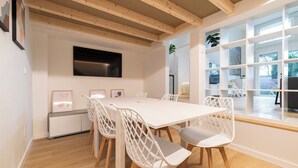 Un comedor moderno con una mesa y sillas blancas, un televisor de pantalla plana en la pared y un ventanal con vistas al exterior.