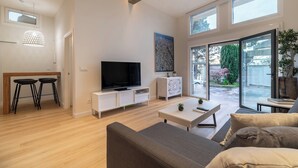 Amplia sala de estar con una televisión de pantalla plana, un sofá, una mesa de centro y un comedor con dos taburetes.