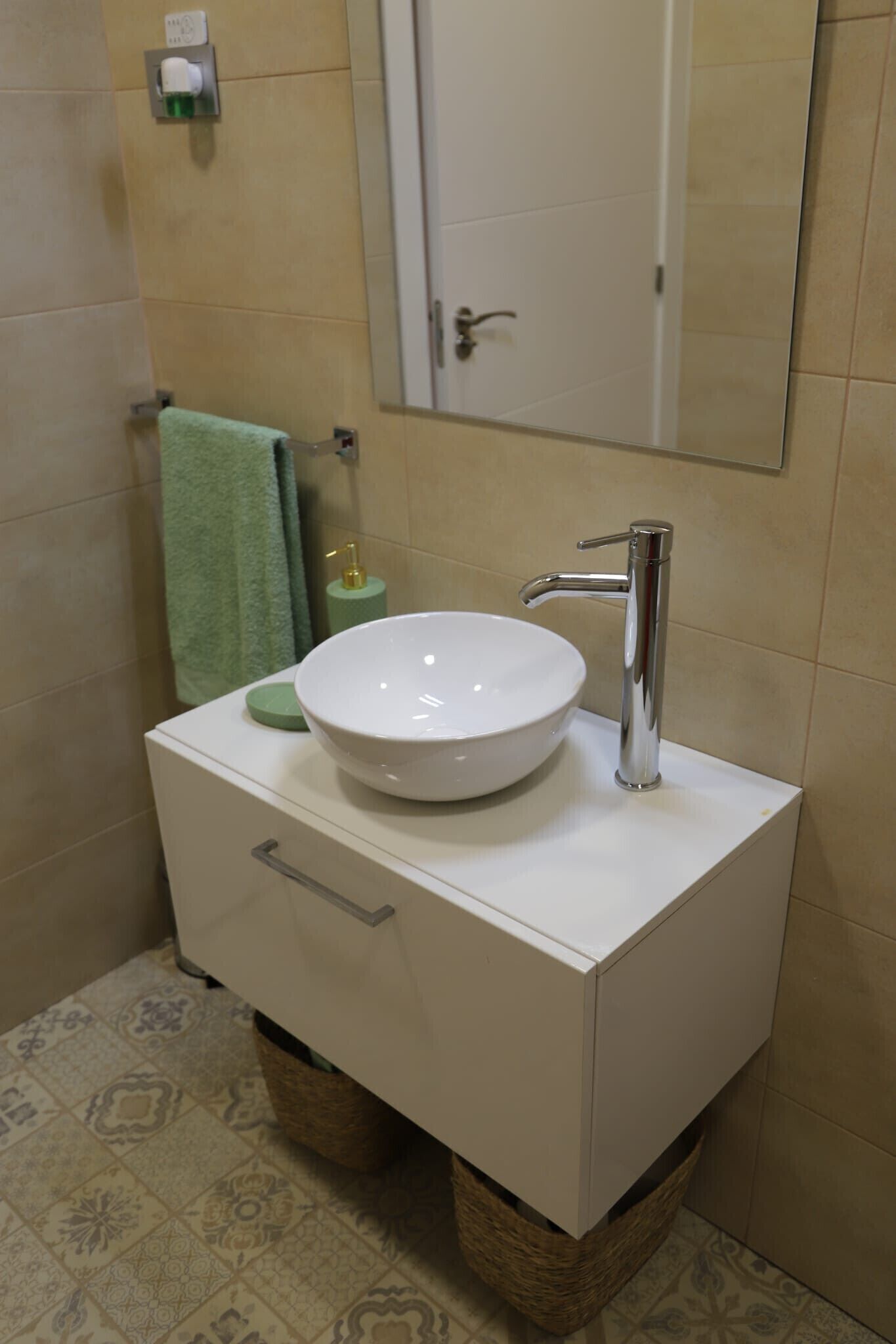 A bathroom with a white vanity, a round sink, a chrome faucet, a mirror, and a green towel.