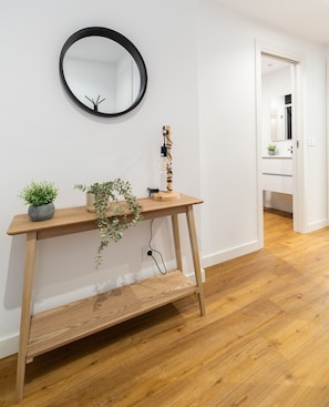 A wooden console table with a mirror, two potted plants, and a lamp with a coiled cord.