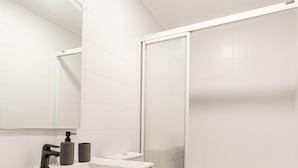 A modern bathroom with a white sink, mirror, and toilet, and a glass-enclosed shower. - Flat Vigo (Vigo)