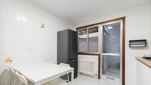 A small kitchen with white tiled walls, a white table with two chairs, a black refrigerator, and a sliding glass door leading to a balcony. - Flat Vigo (Vigo)