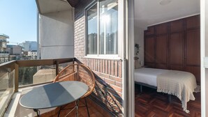 A balcony with a table and chair, a bed with a white bedspread, and a wooden wardrobe. - Flat Vigo (Vigo)
