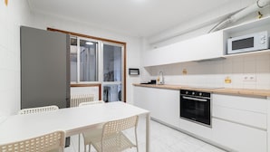 A modern kitchen with white cabinetry, a microwave, an oven, and a dining area with a table and chairs. - Flat Vigo (Vigo)