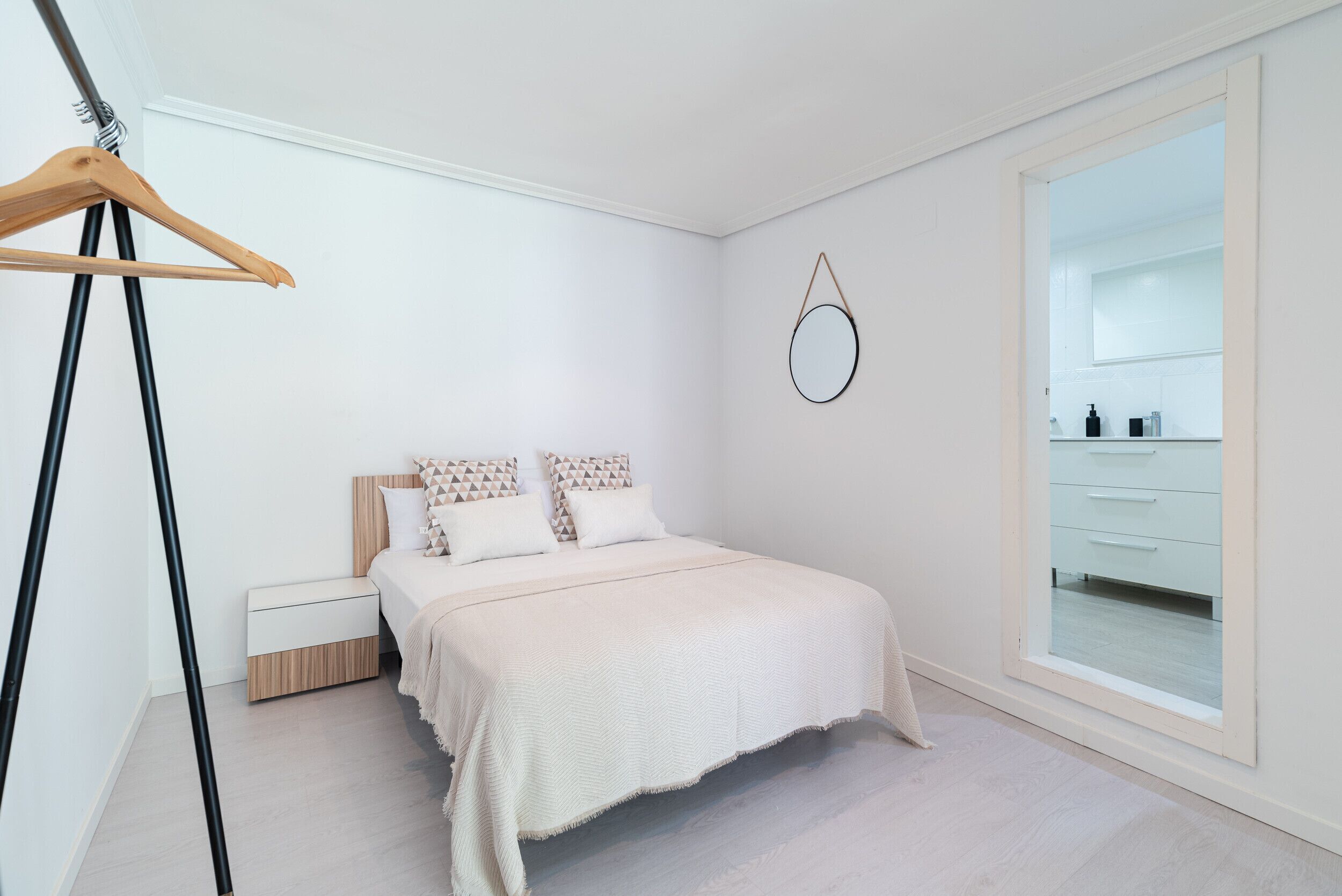 A bedroom with a bed, a bedside table, a hanging mirror, and a wardrobe.