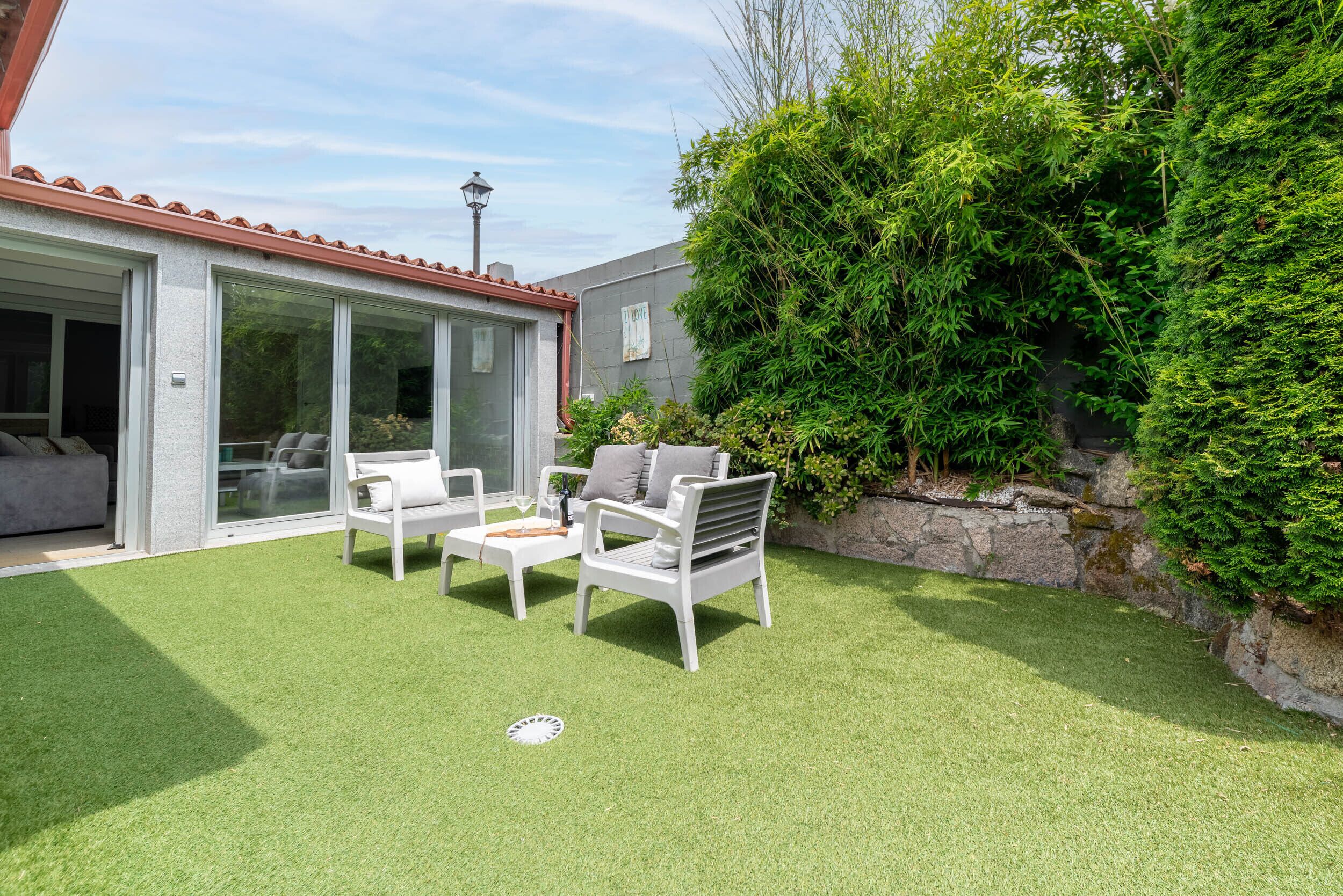 A patio with artificial grass, white outdoor furniture, and a stone wall with greenery.