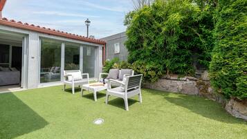 A patio with artificial grass, white outdoor furniture, and a stone wall with greenery.