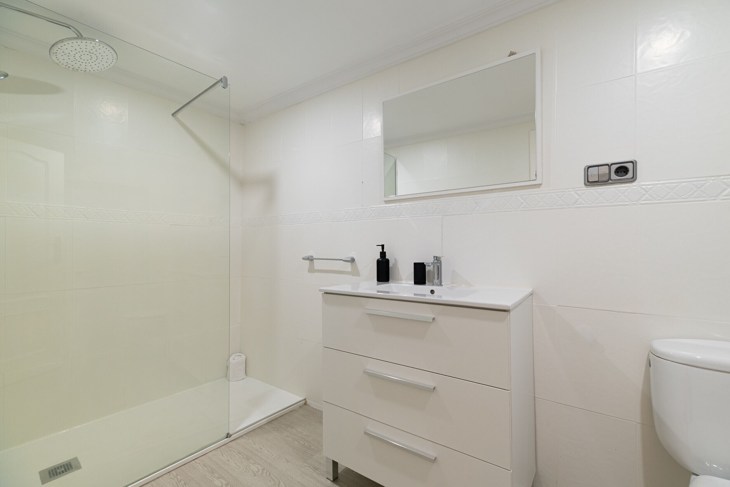 A bathroom with a glass shower enclosure, a white sink with a mirror above it, and a toilet.