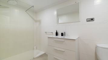 A bathroom with a glass shower enclosure, a white sink with a mirror above it, and a toilet.