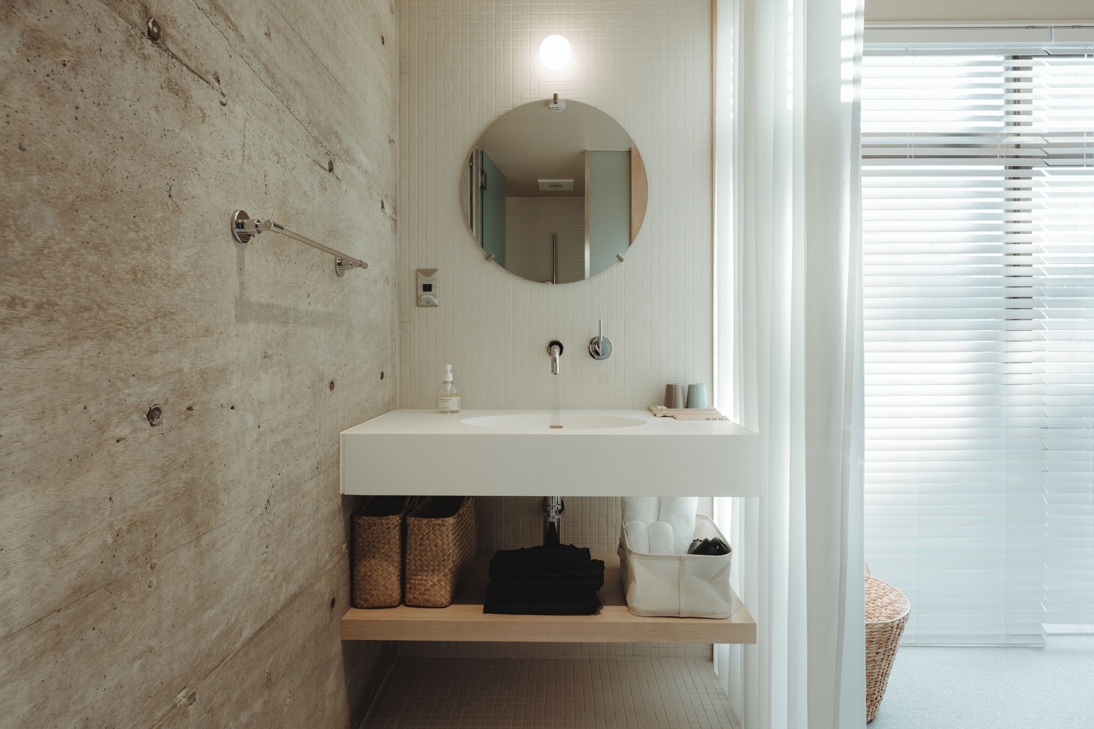 Un baño moderno con una pared de acento de madera, un espejo redondo, un lavabo blanco y un estante pequeño con cestas.